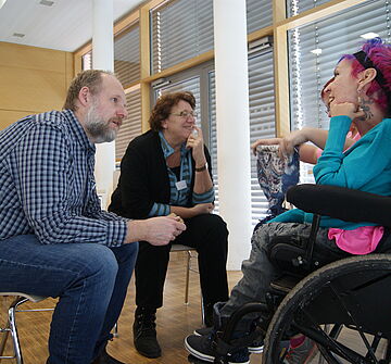 Pflegekräfte im Gespräch mit einer Frau mit Rollstuhl